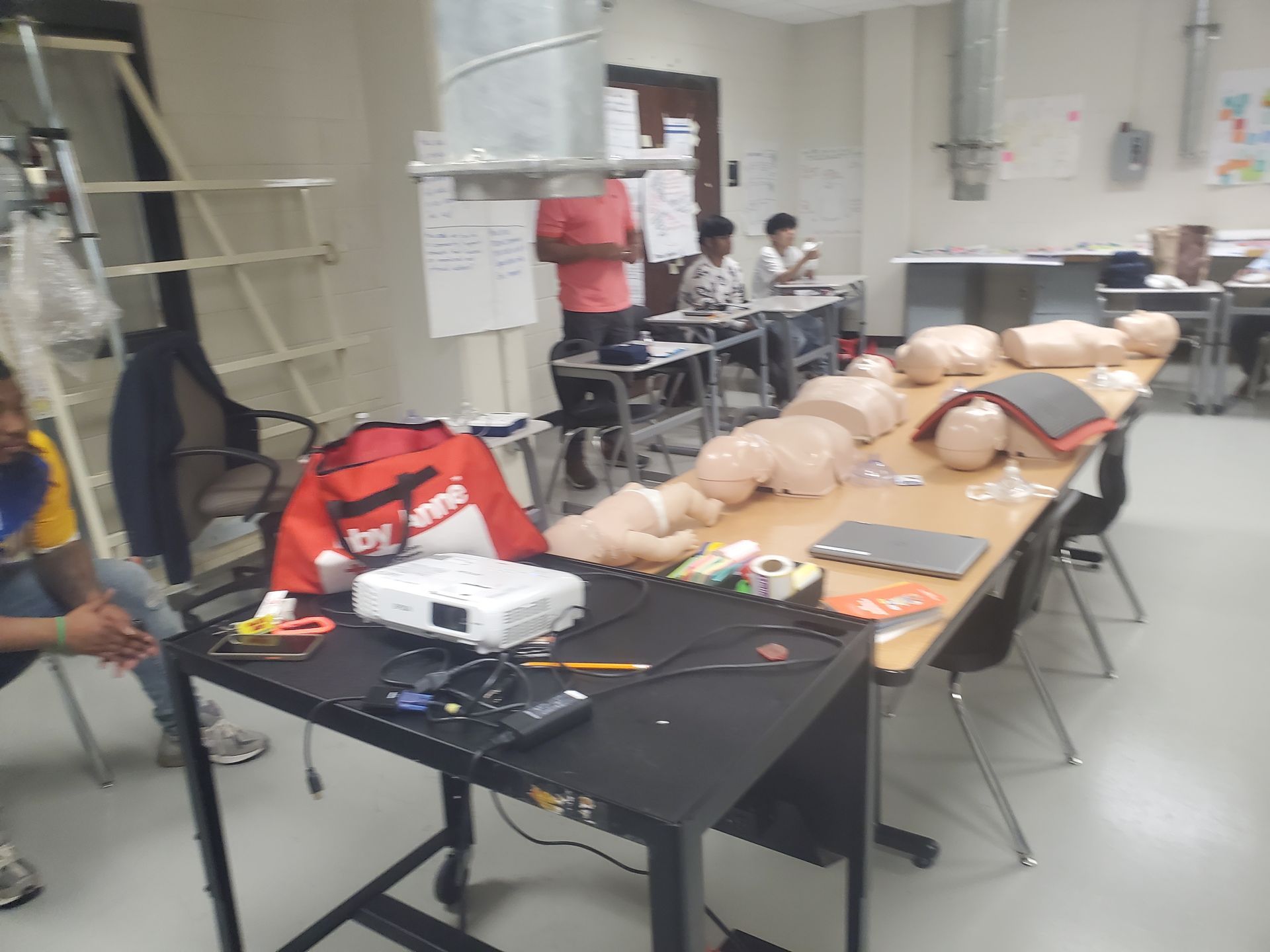 A group of people are sitting at tables in a room with a bag that says supreme on it