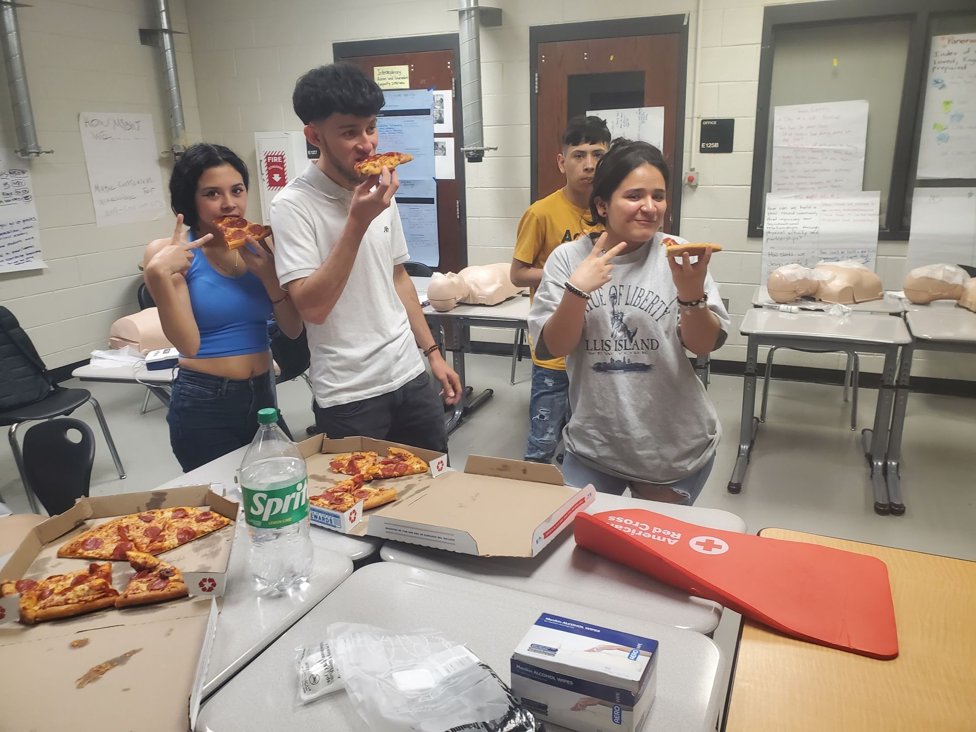 A group of people are eating pizza in a classroom.