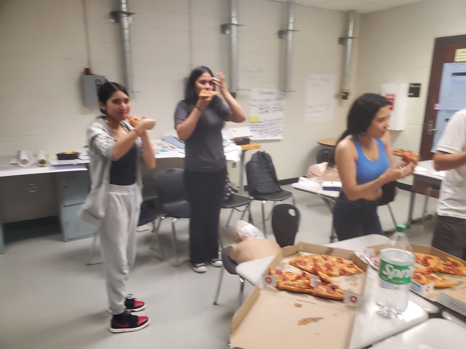 A group of people standing around a table with pizza and a sprite bottle