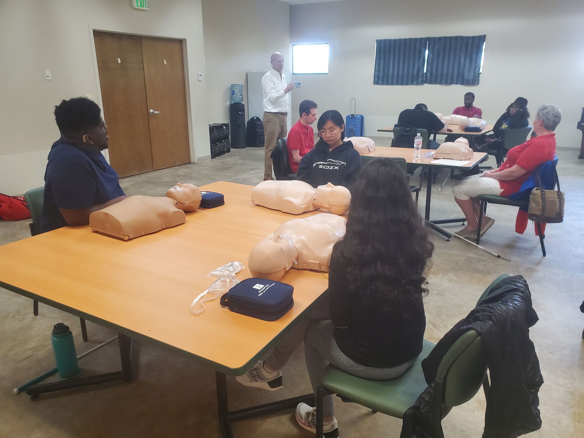 A group of people are sitting at tables with mannequins on them.