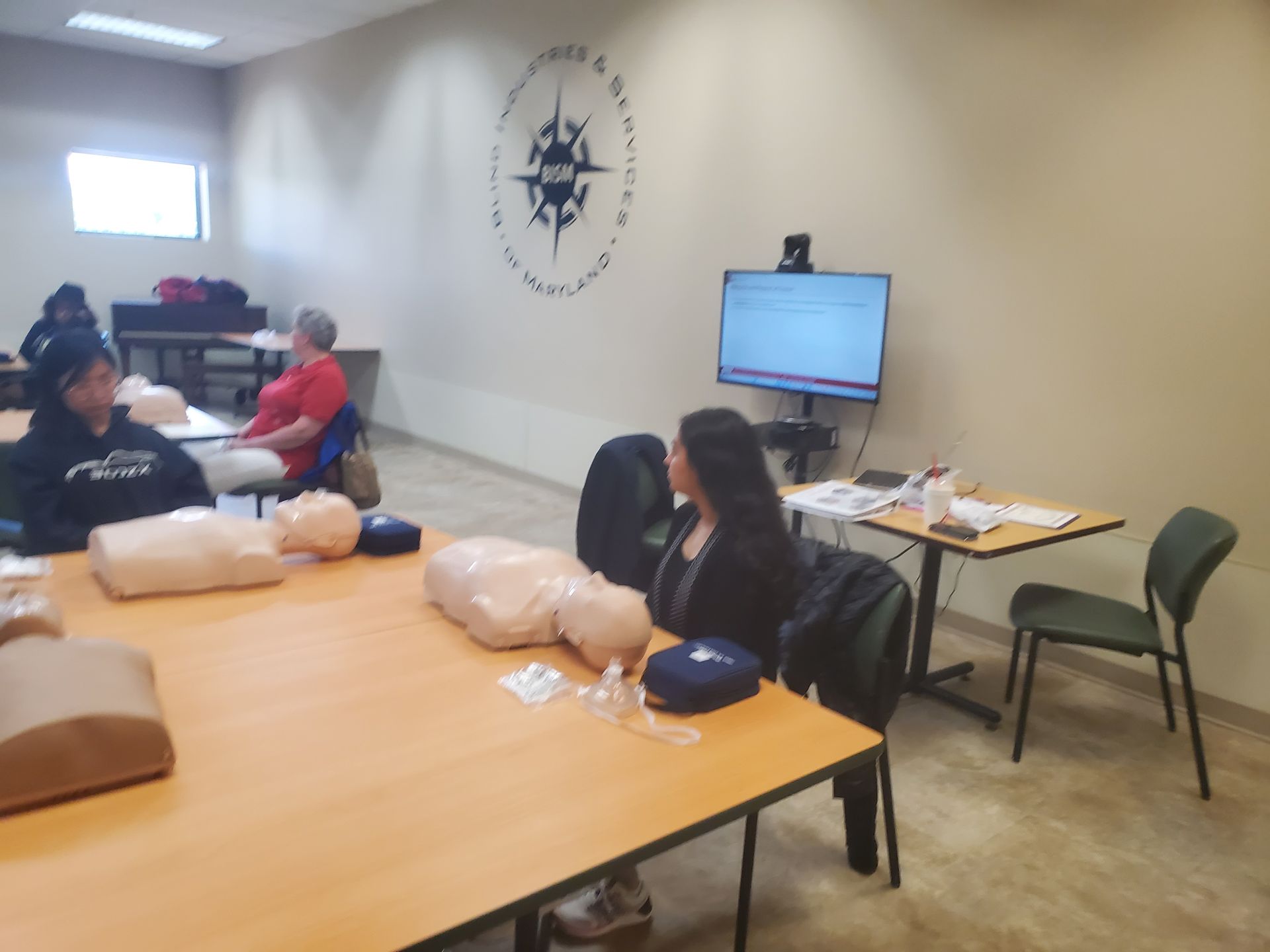 A group of people are sitting at tables in a room with a compass on the wall.