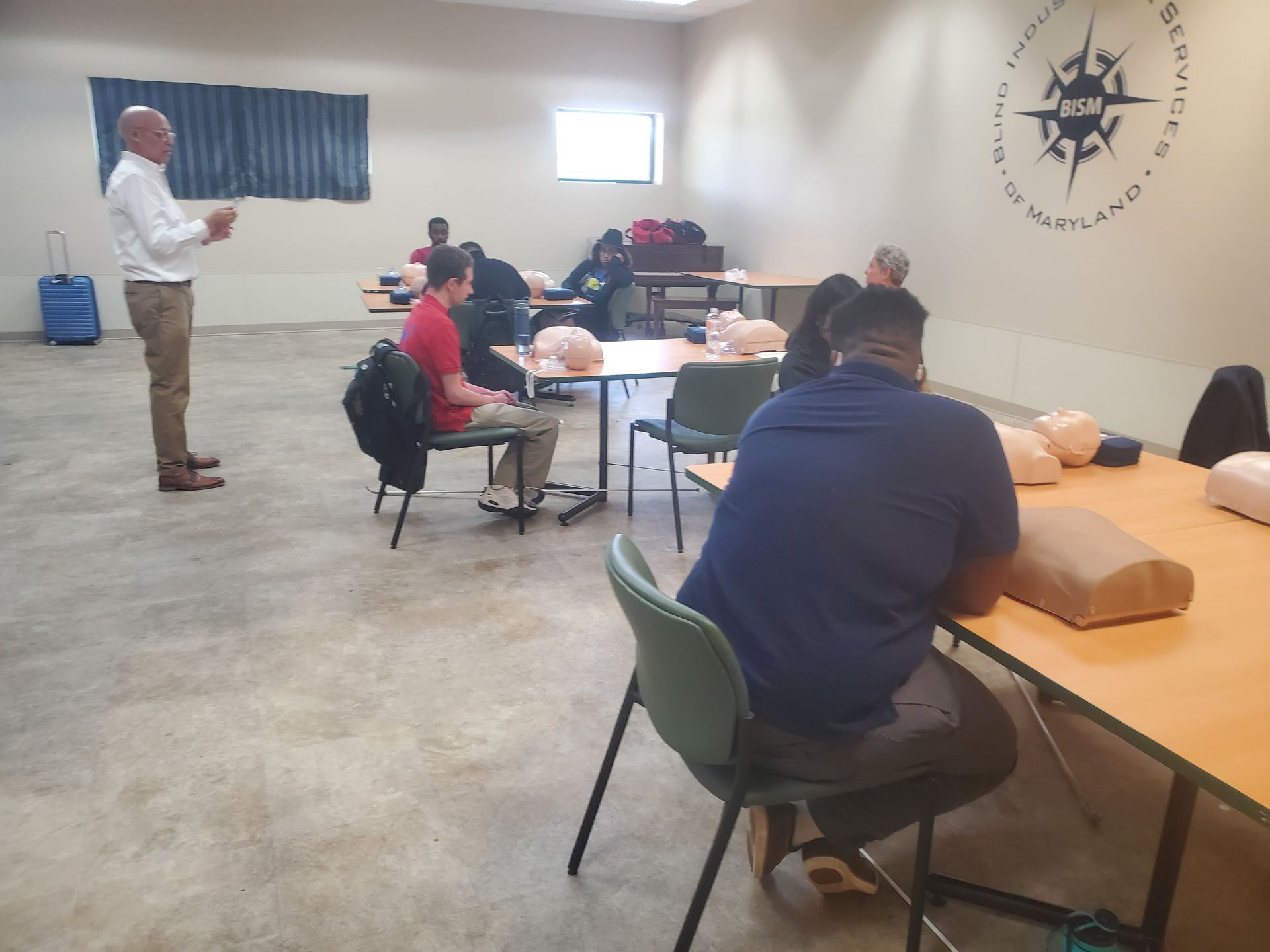 A group of people are sitting at tables in a room with a compass on the wall.