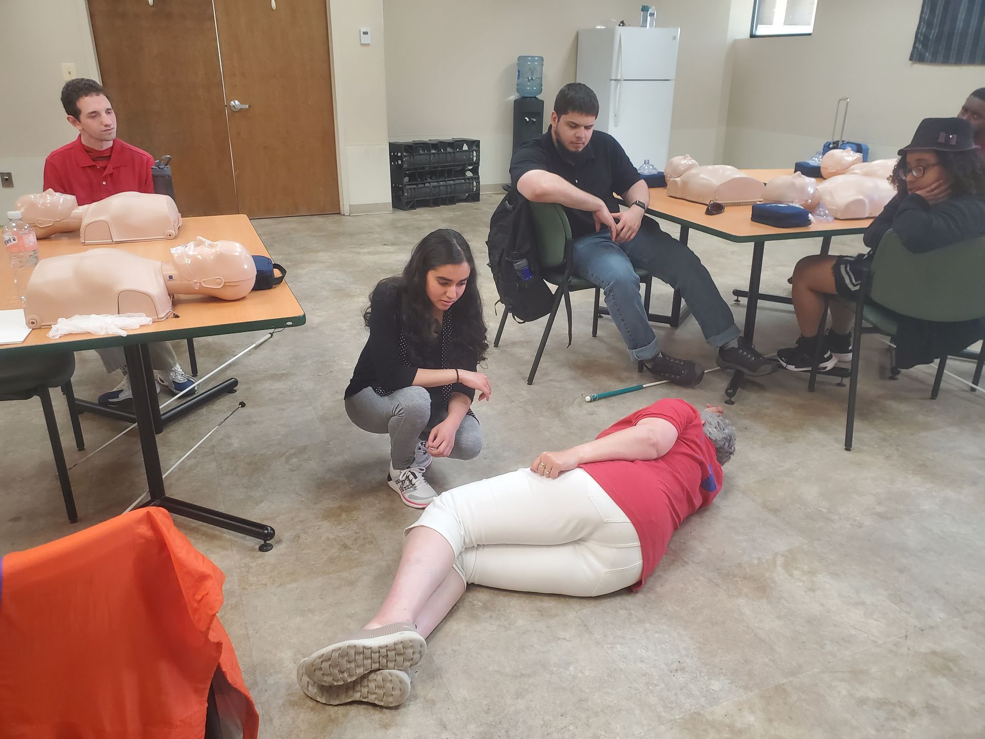 A group of people are sitting around tables and a woman is laying on the floor.