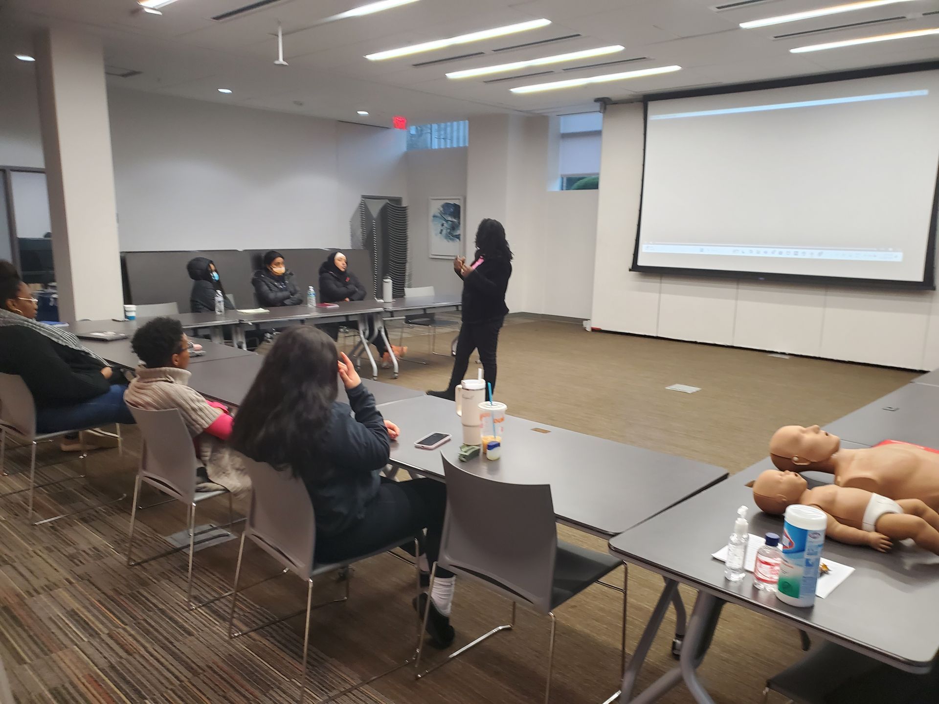 A group of people are sitting at tables in front of a projector screen.