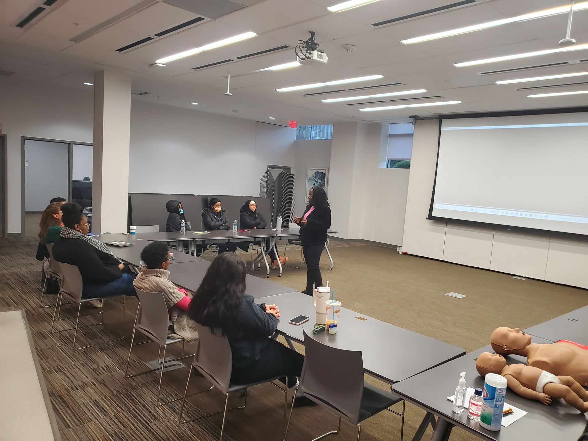 A group of people are sitting at tables in a room with a projector screen.