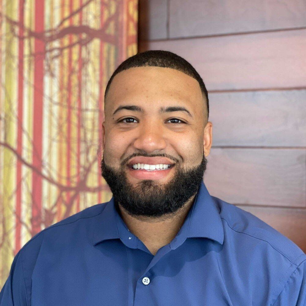 A man with a beard is wearing a blue shirt and smiling for the camera.