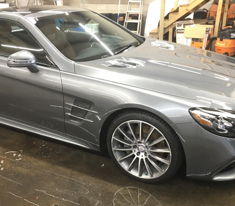 A sleek grey Mercedes-Benz coupe parked inside a garage, highlighting its side profile, wheels, and front hood.