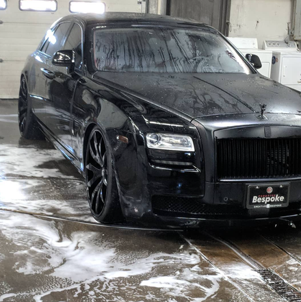 A shiny black Rolls-Royce Ghost parked in a car wash bay with soap suds on the floor.