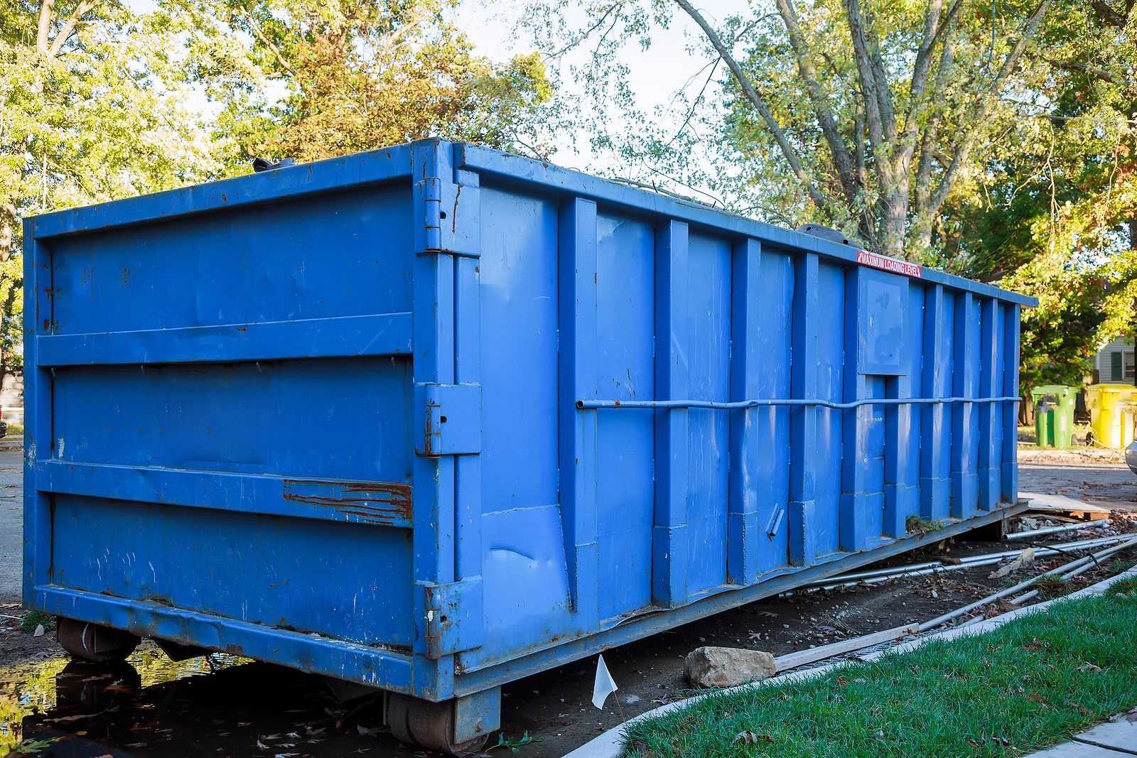 A large blue dumpster is parked in the grass in a yard.