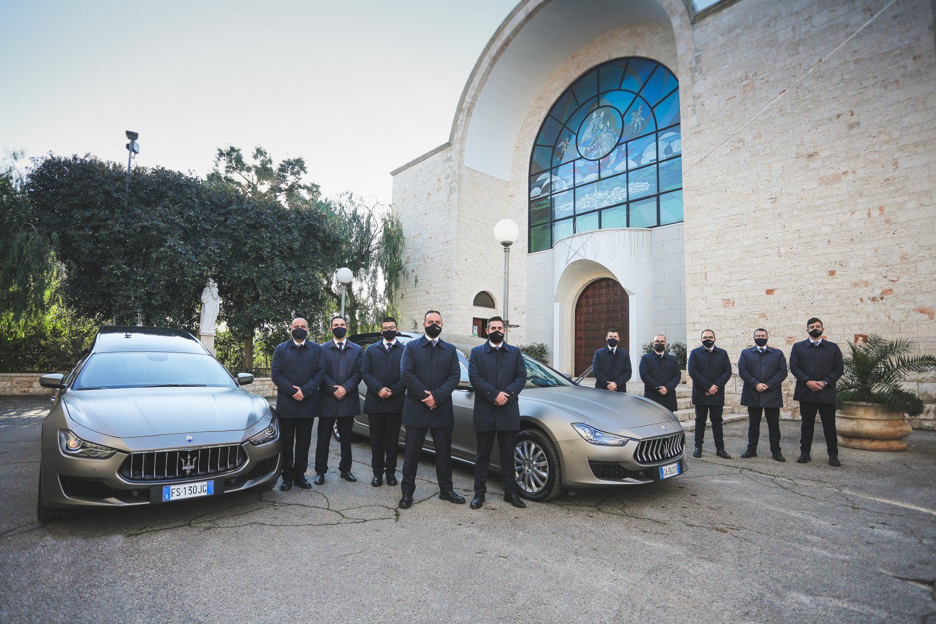 Un gruppo di uomini in piedi accanto a due auto di fronte a un edificio.