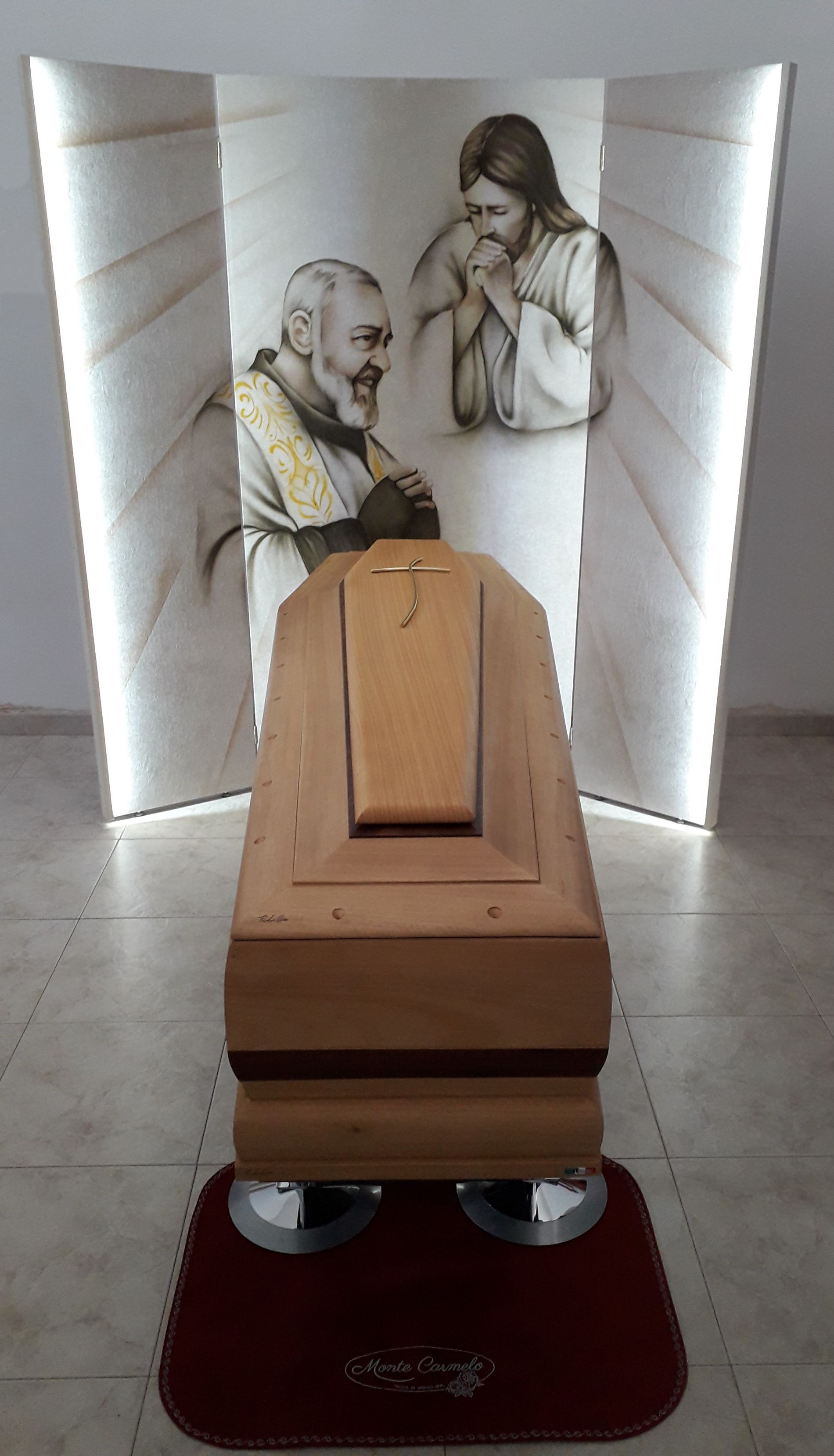 Una bara di legno è posta davanti a un dipinto di Gesù e Padre Pio.