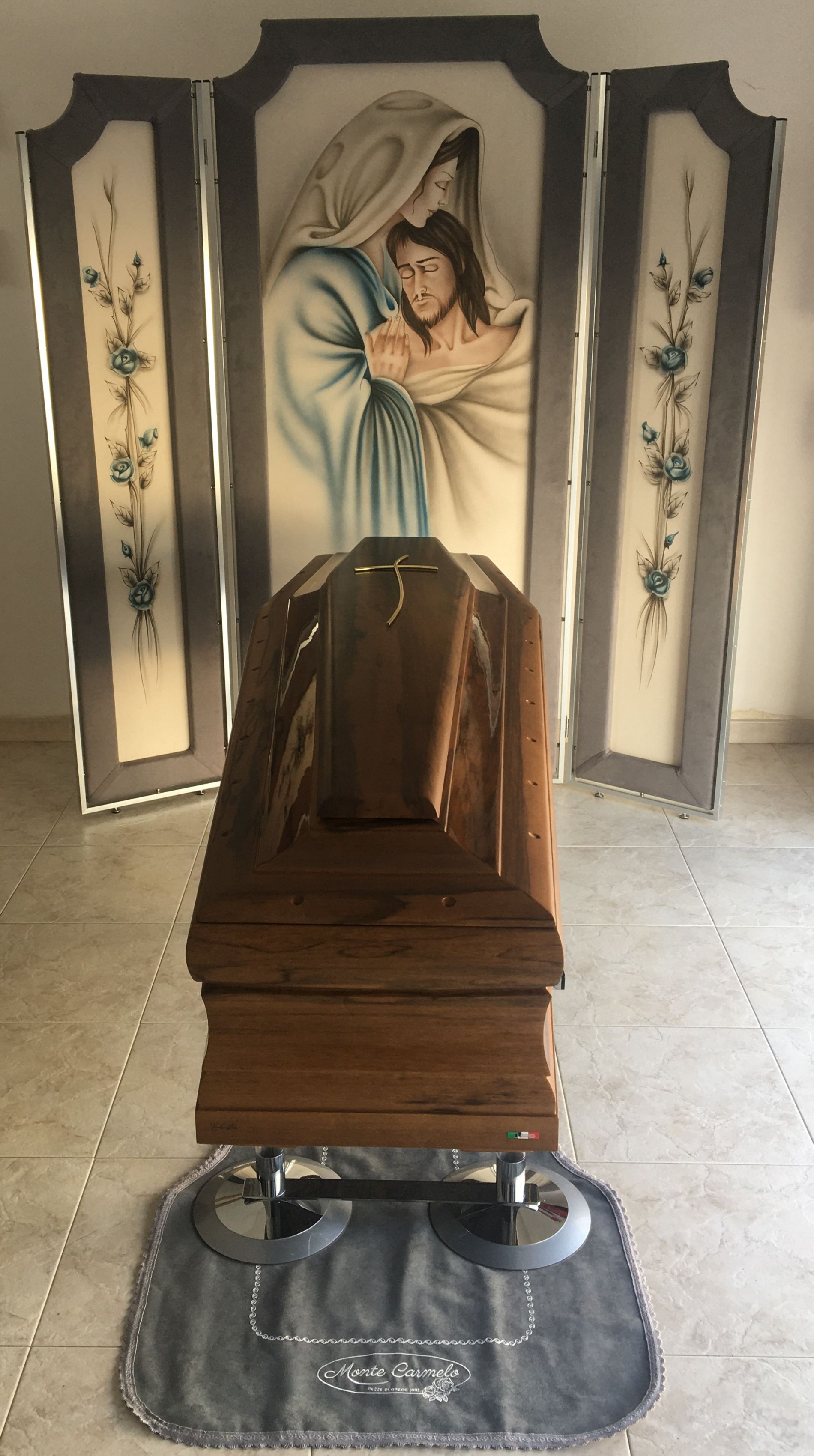 Una bara di legno è posta davanti a un dipinto di Gesù e Maria.