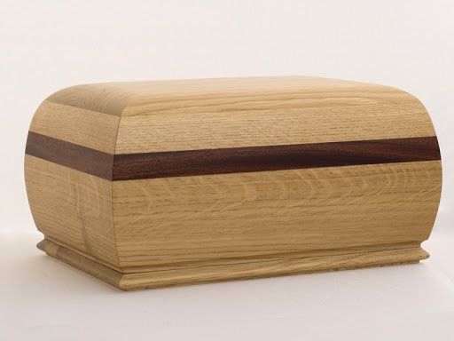 Una scatola di legno con una striscia marrone sul lato è appoggiata su una superficie bianca.