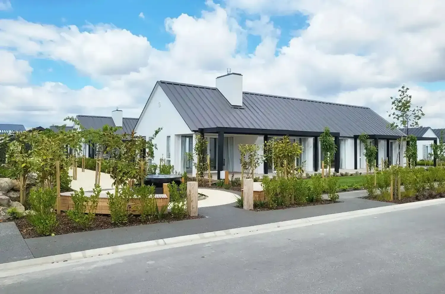 White, modern house with dark gray roof; landscaped garden in front. Sunny, outdoor setting.