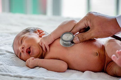 2 week old baby lying in a crip with a hand holding a stethoscope over its chest.