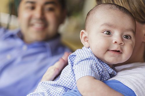 6 month old baby on the shoulder of an adult.