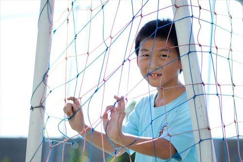 Boy smiling, holding soccer net, outdoors.