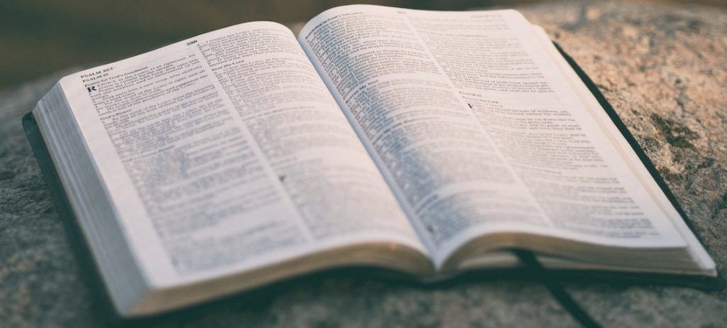 Open Bible on a stone surface, pages illuminated by sunlight.