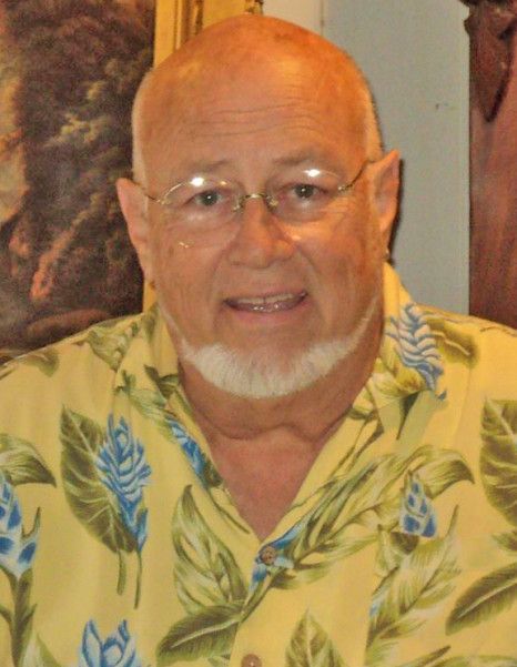A person with a white goatee, wearing thin-rimmed glasses and a yellow short-sleeved shirt with a blue leaf pattern.