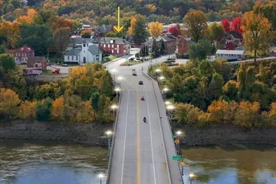 An aerial view of a road leading from a river across a bridge to a small town surrounded by colorful autumn trees.