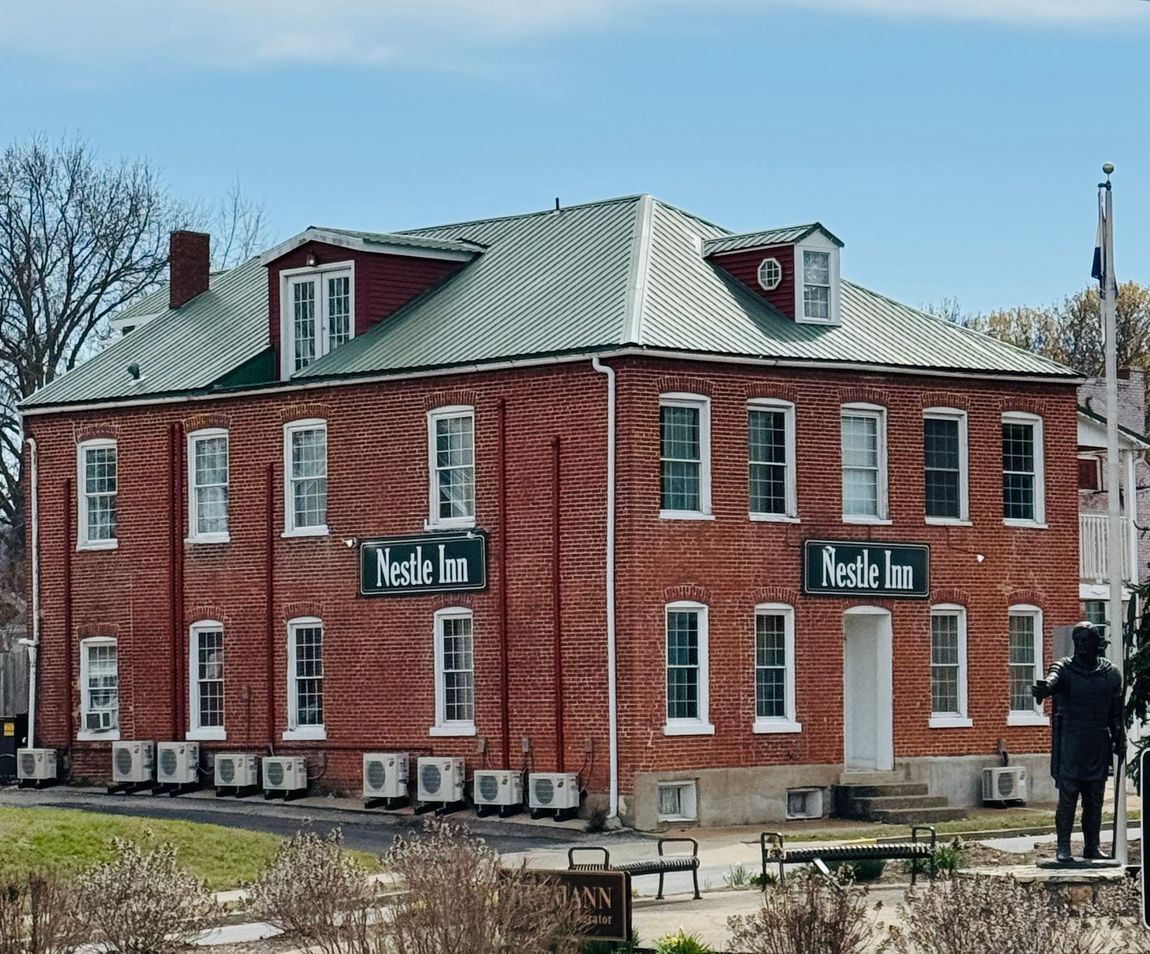 A two-story red brick building with a green metal roof labeled 