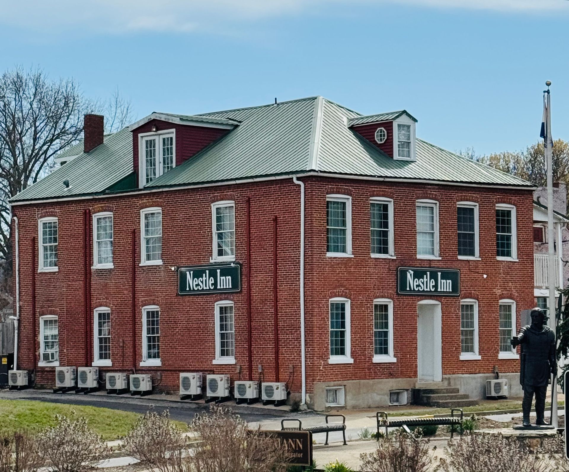 A two-story red brick building with a green metal roof labeled