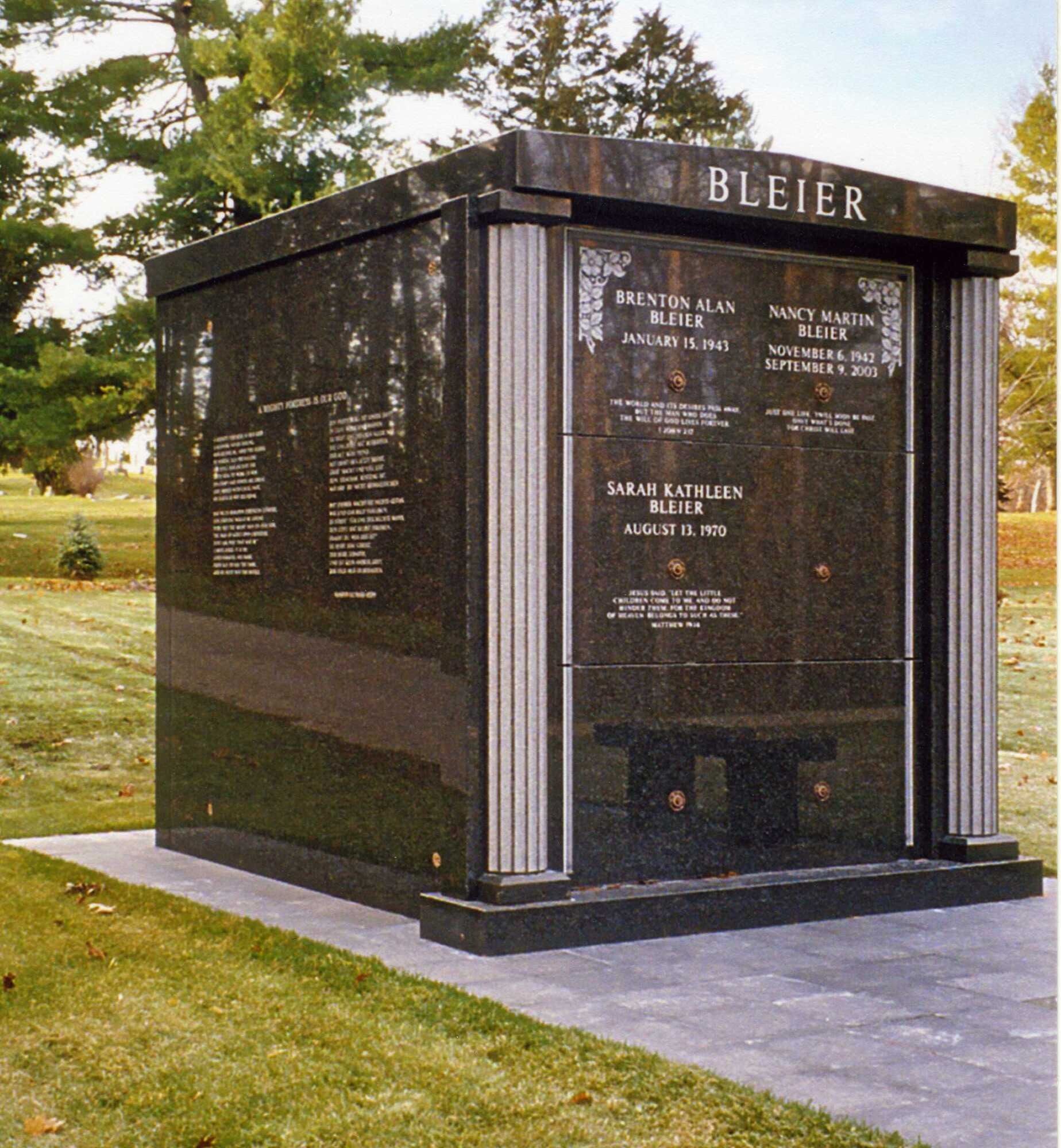 Black granite memorial wall engraved with names, standing on a lawn at a cemetery or park.