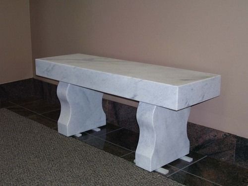 Stone bench with curved supports on a tiled floor against a plain wall