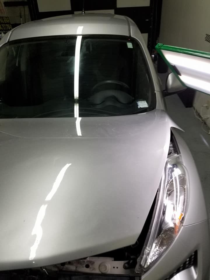 A silver car with the hood up is parked in a garage.