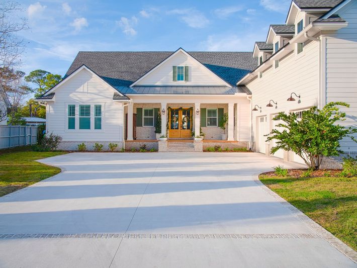 White house with a covered porch and a long driveway, under a blue sky.