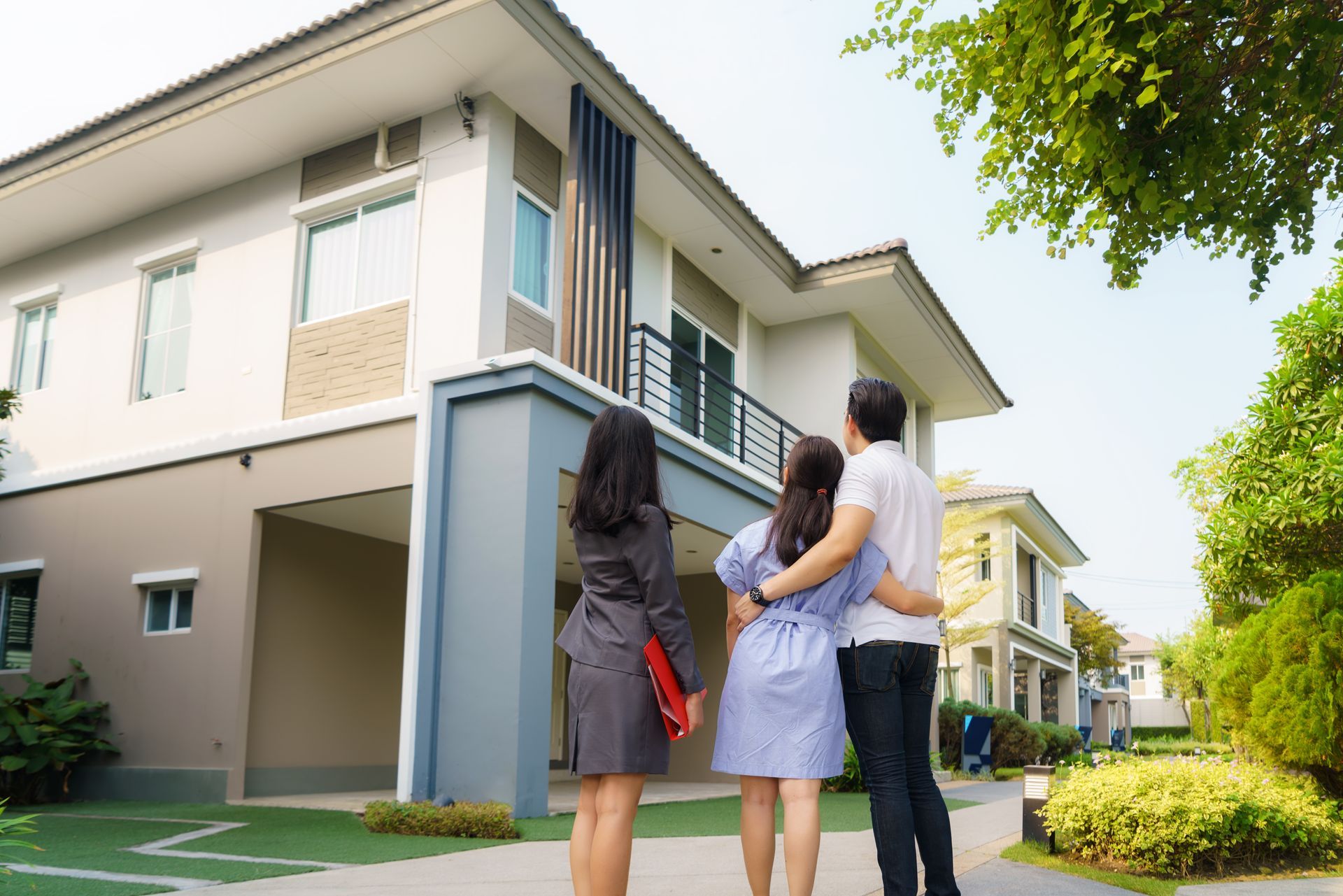Real estate agent showing a couple a two-story house; sunny day.