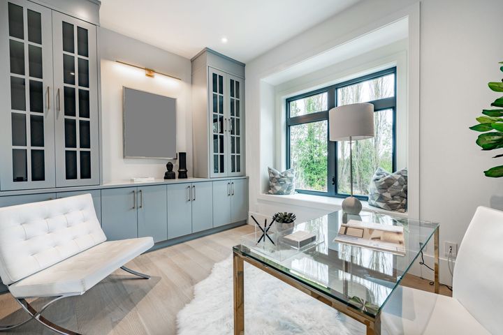 Light blue office with desk, modern chair, built-in storage, and window seat with pillows.