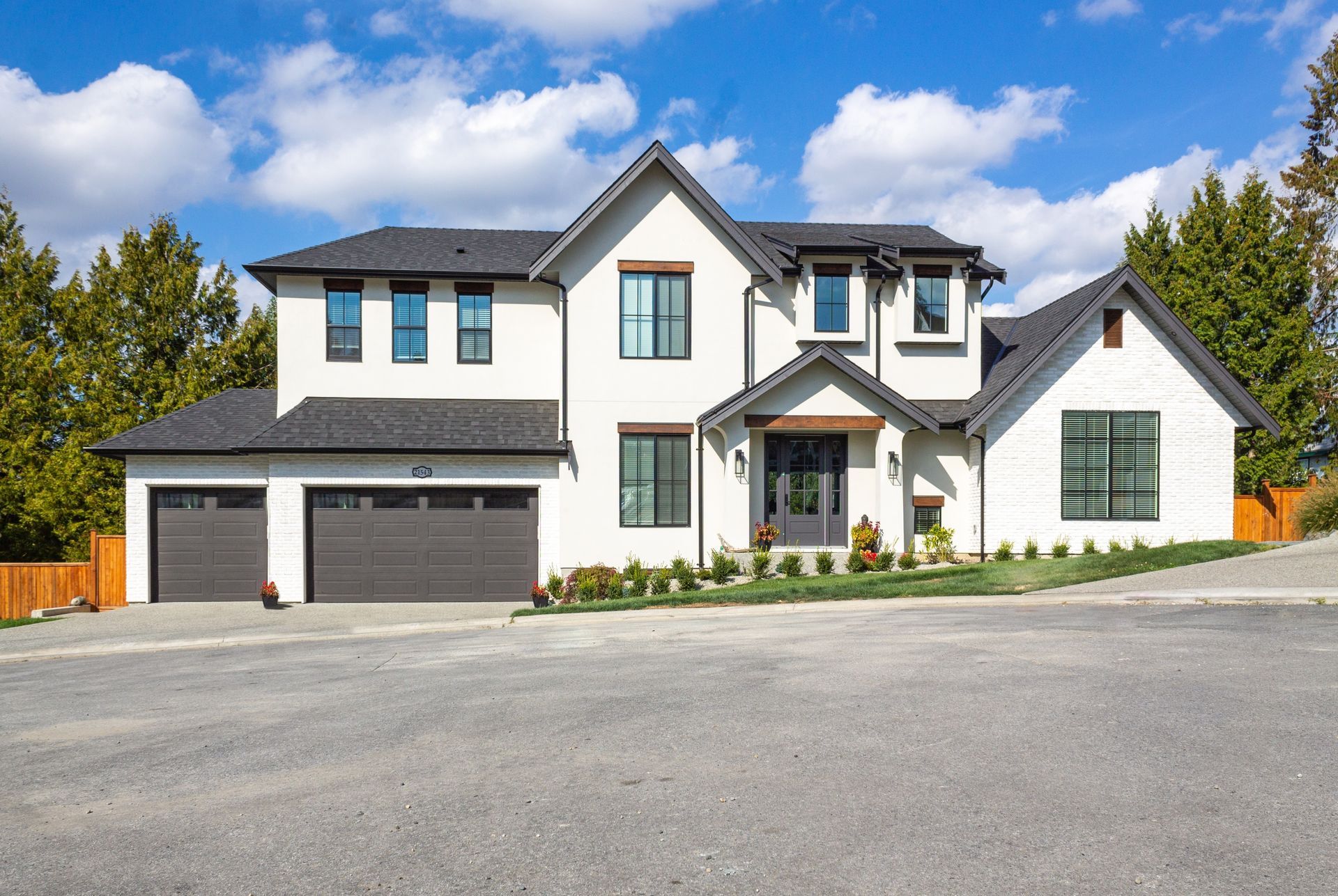 Two-story white house with dark gray roof, garage doors, and trim; blue sky.