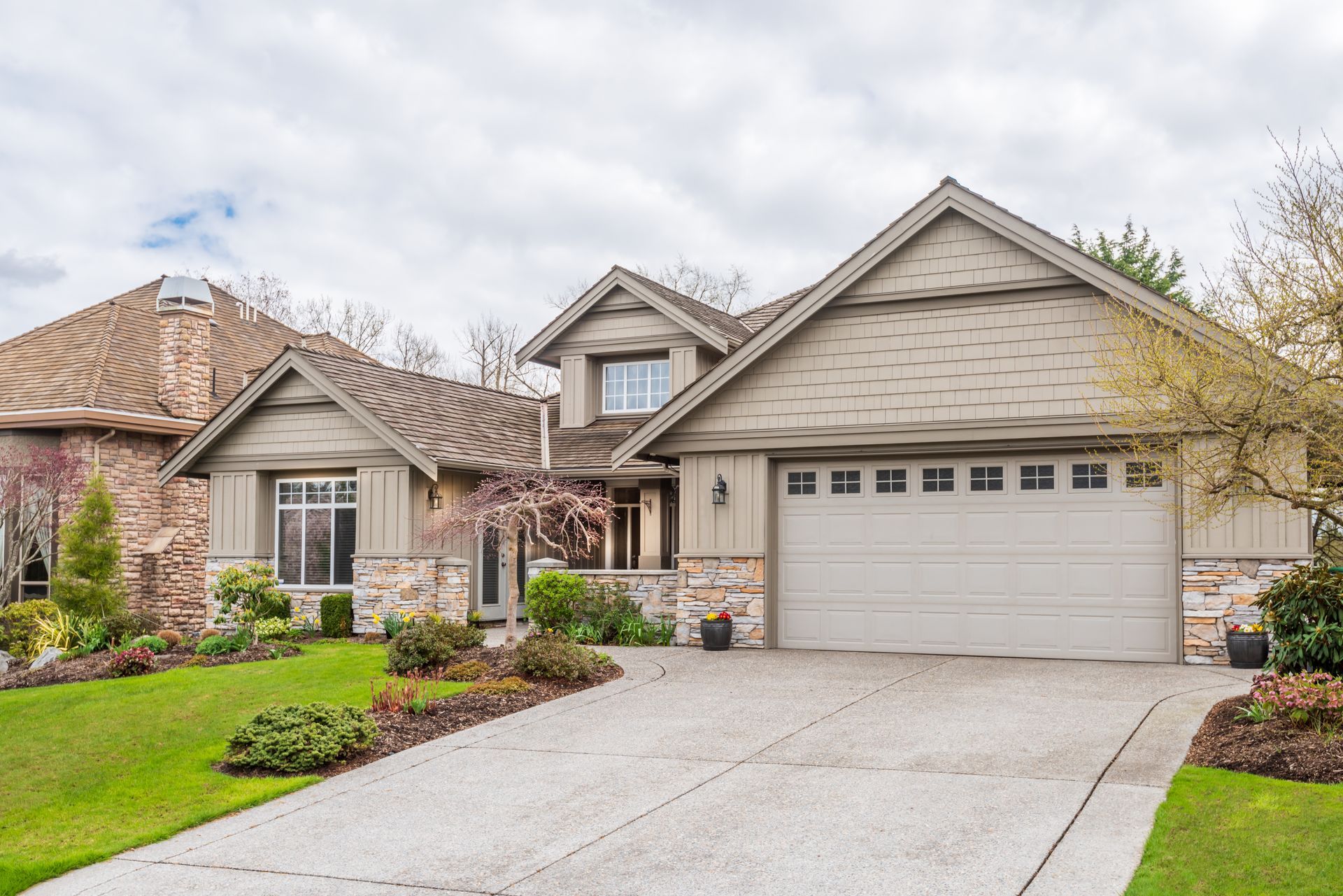House with beige siding, stone accents, attached garage, and a concrete driveway.