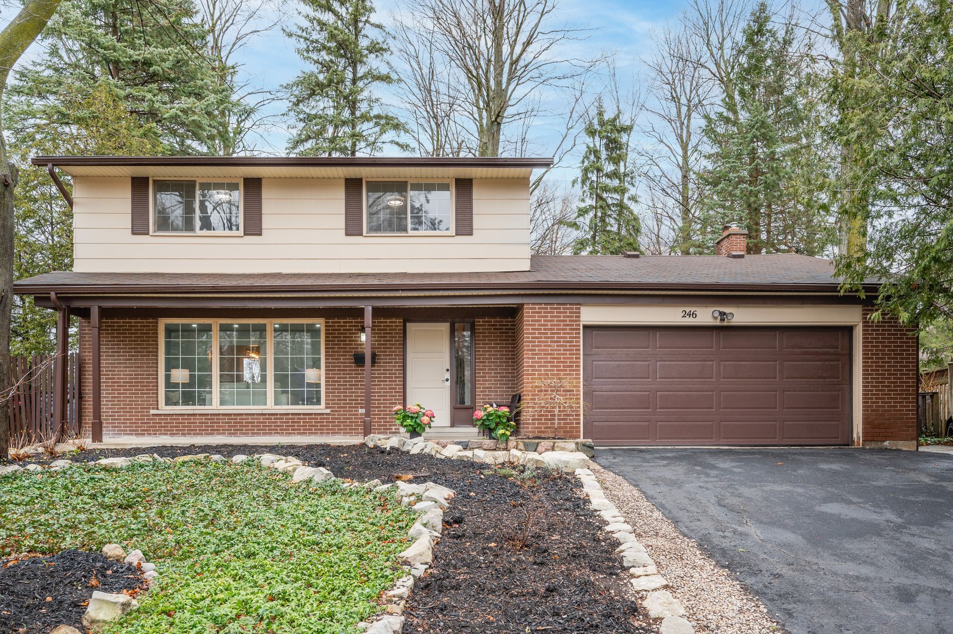 Two-story house with tan siding, brown shutters, brick accents, and a brown garage door.
