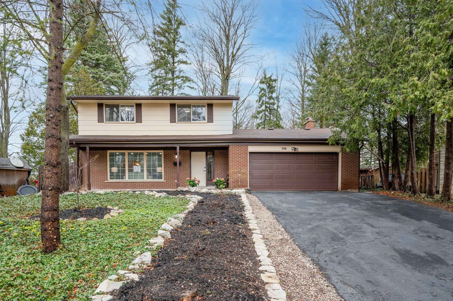 Two-story house with brown garage door, driveway, and front path lined with plants.