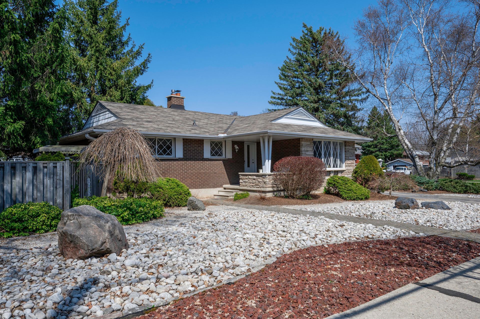 Brick bungalow with stone landscaping and gray gravel yard on a sunny day.