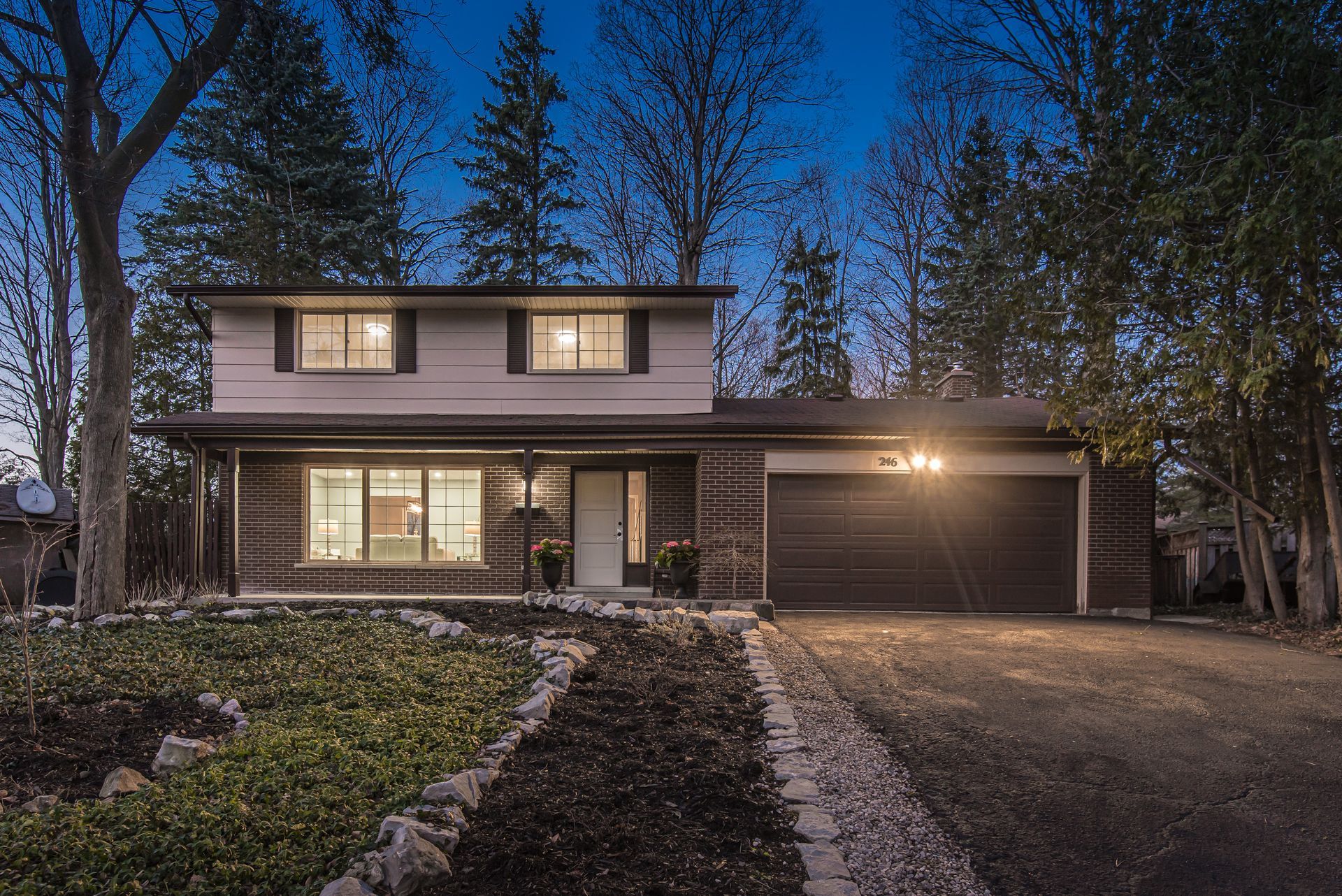 Two-story house at dusk, with lights on. Features a brick facade, garage, and a landscaped front yard.