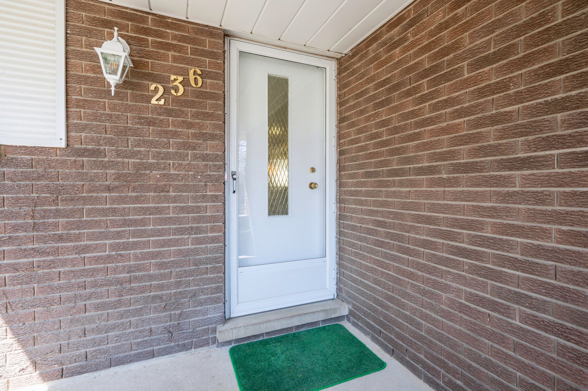 White front door with glass panel, brick walls, green welcome mat, and address 236.