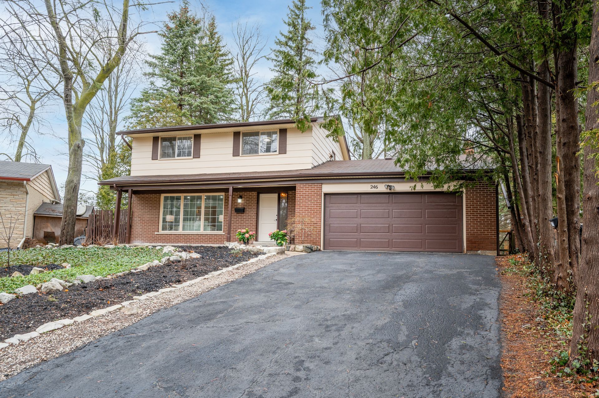 Two-story house with brown garage door and brick facade, asphalt driveway, and trees.