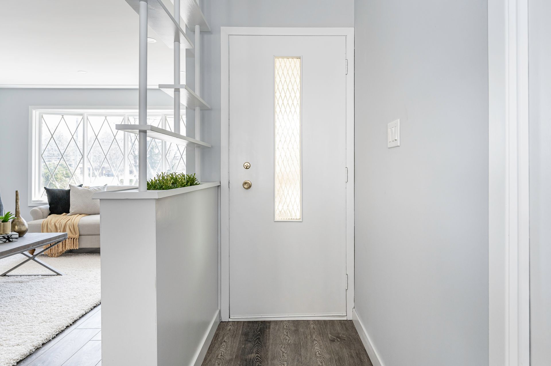 Hallway with white door and sidelight, leading to living room with neutral decor.