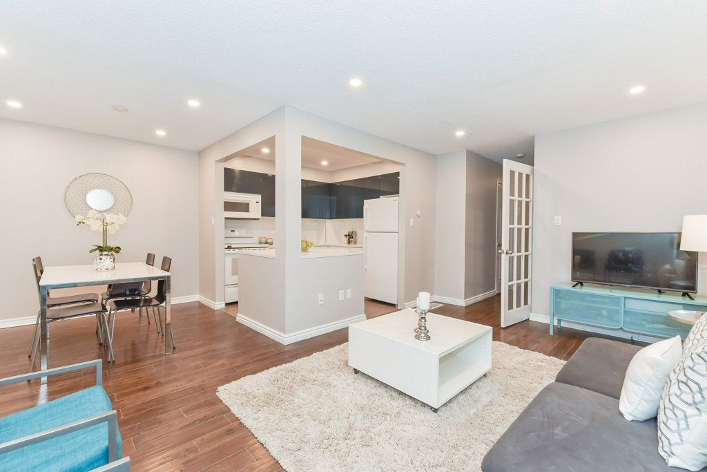 Modern living room with open kitchen. White walls, wood floor, teal accents.