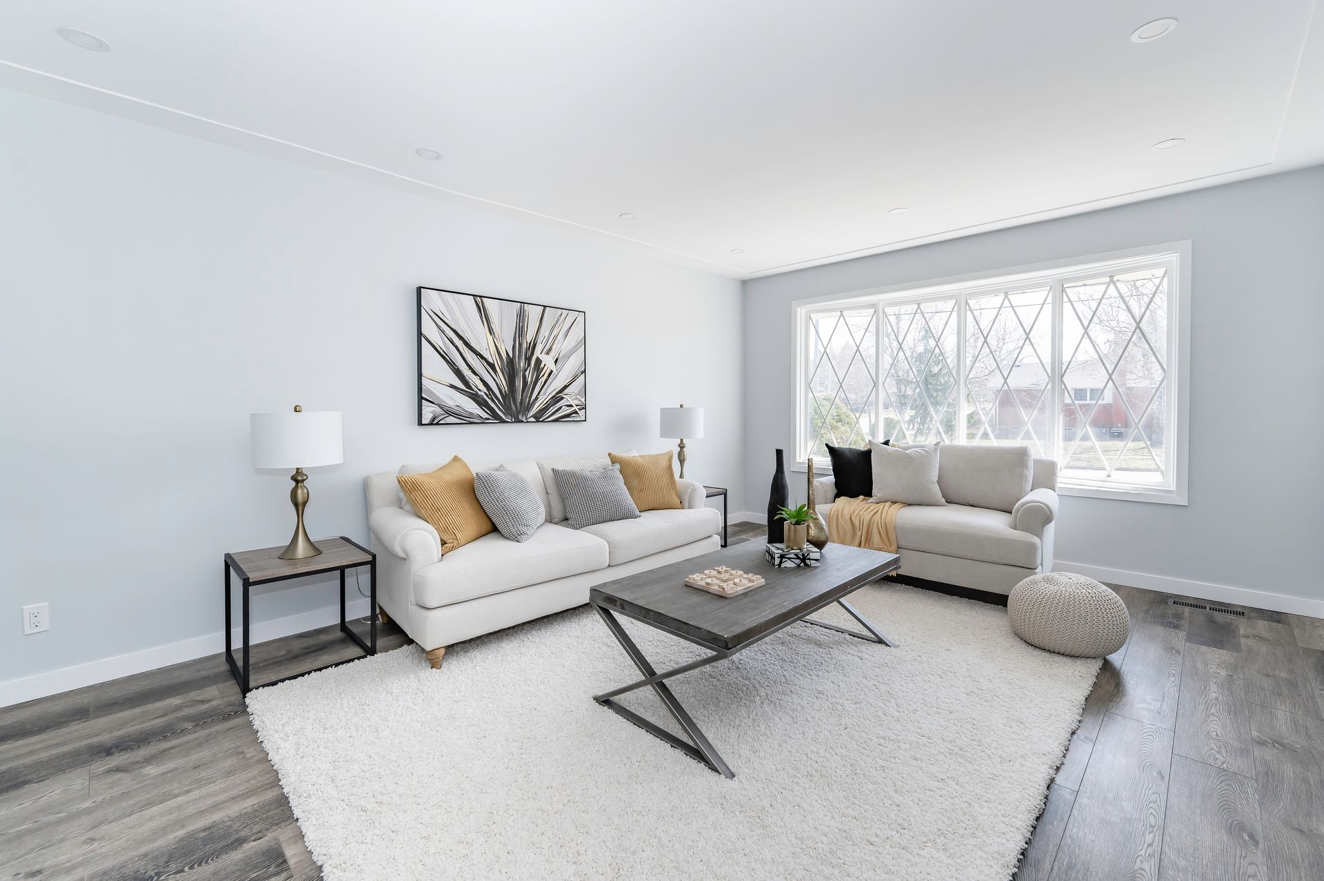 Living room with white sofa, rug, and light gray walls; decorated with pillows, lamp, and artwork.