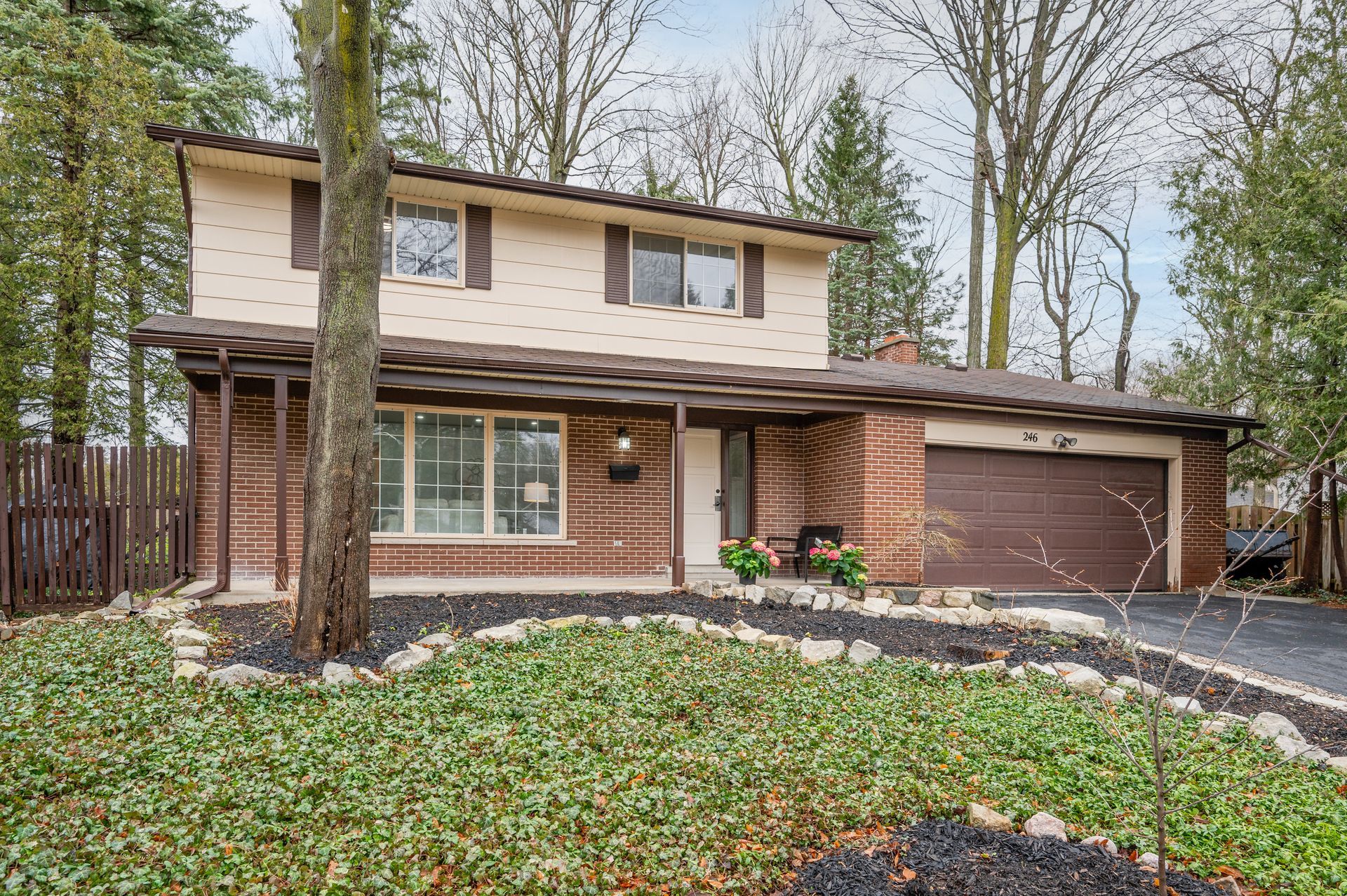 Two-story brick house with a brown garage door and front yard landscaping under a cloudy sky.