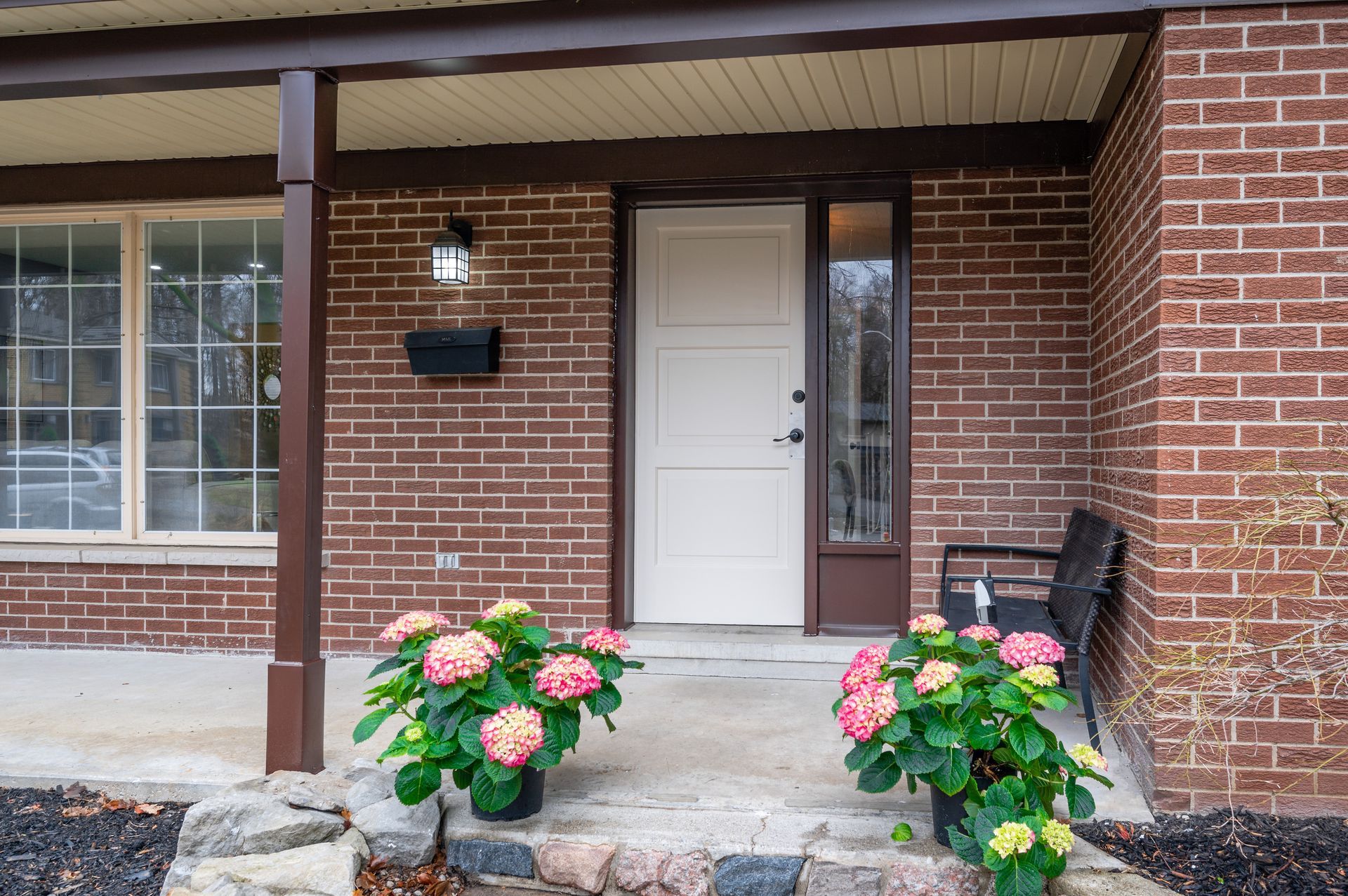 Brick house exterior with white door, porch, pink flowers, and a black mailbox.