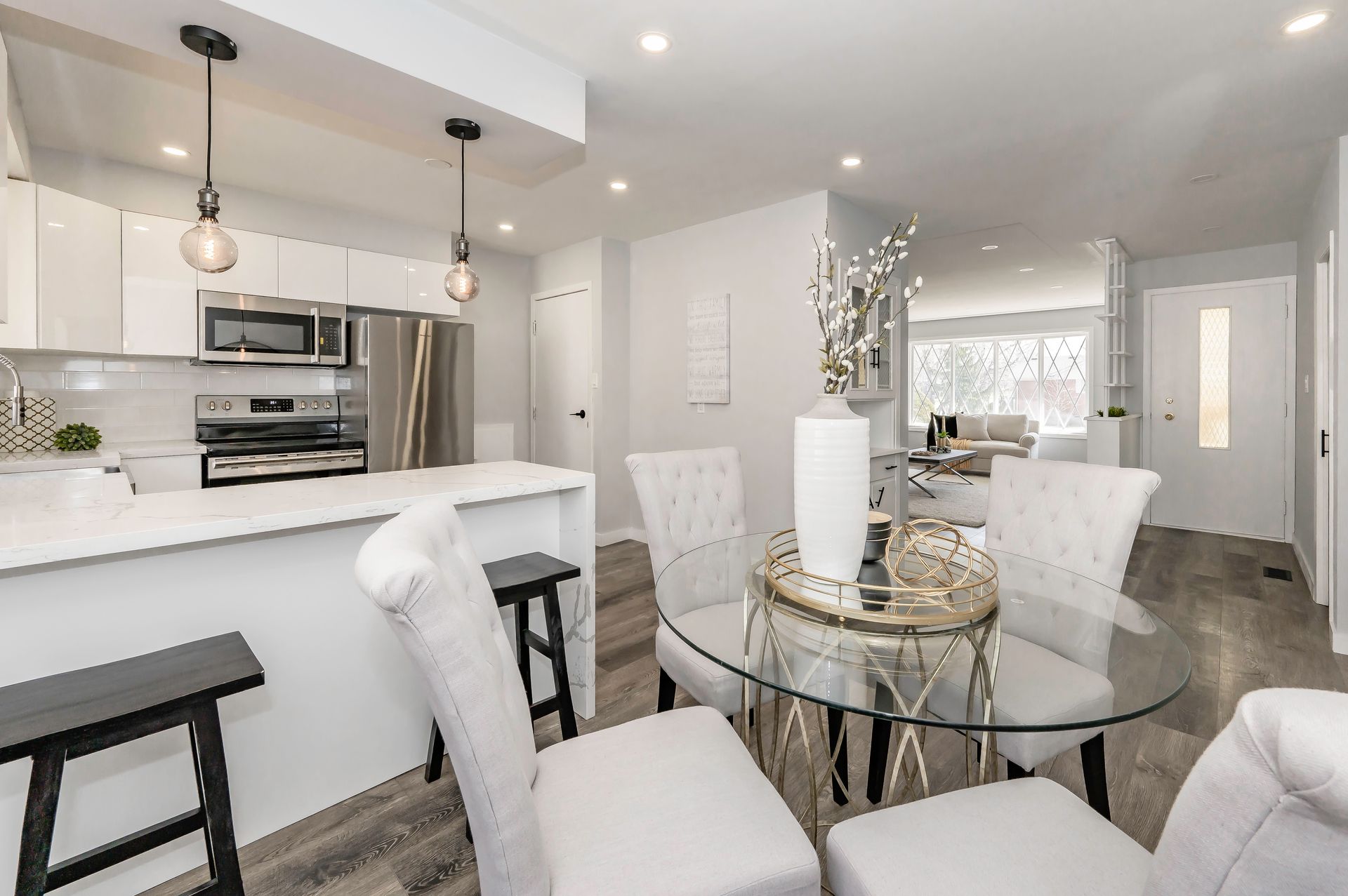 Modern kitchen and dining area with white cabinets, stainless steel appliances, and a glass-top table.