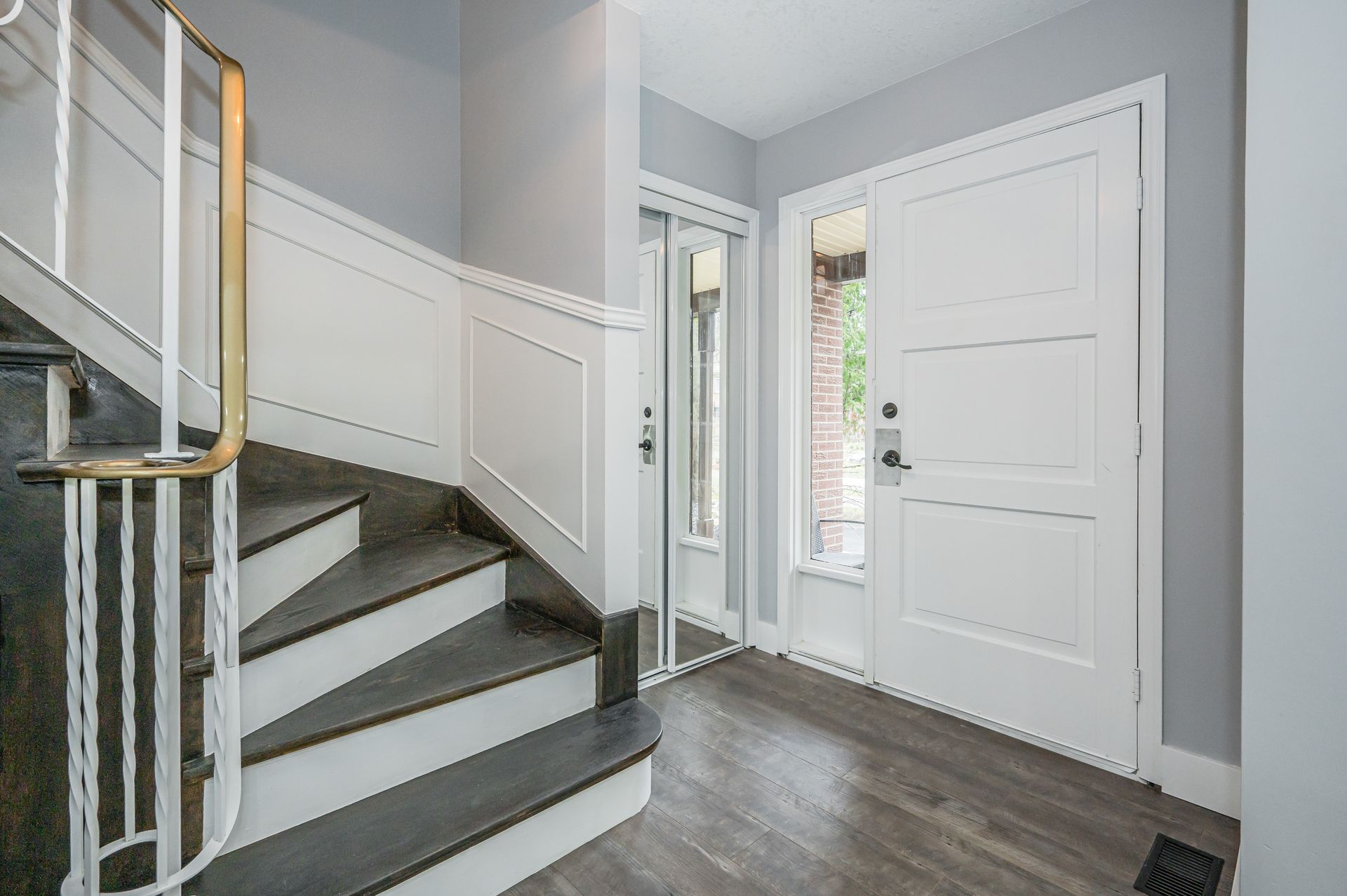Entryway with staircase and white door, dark flooring and gray walls.