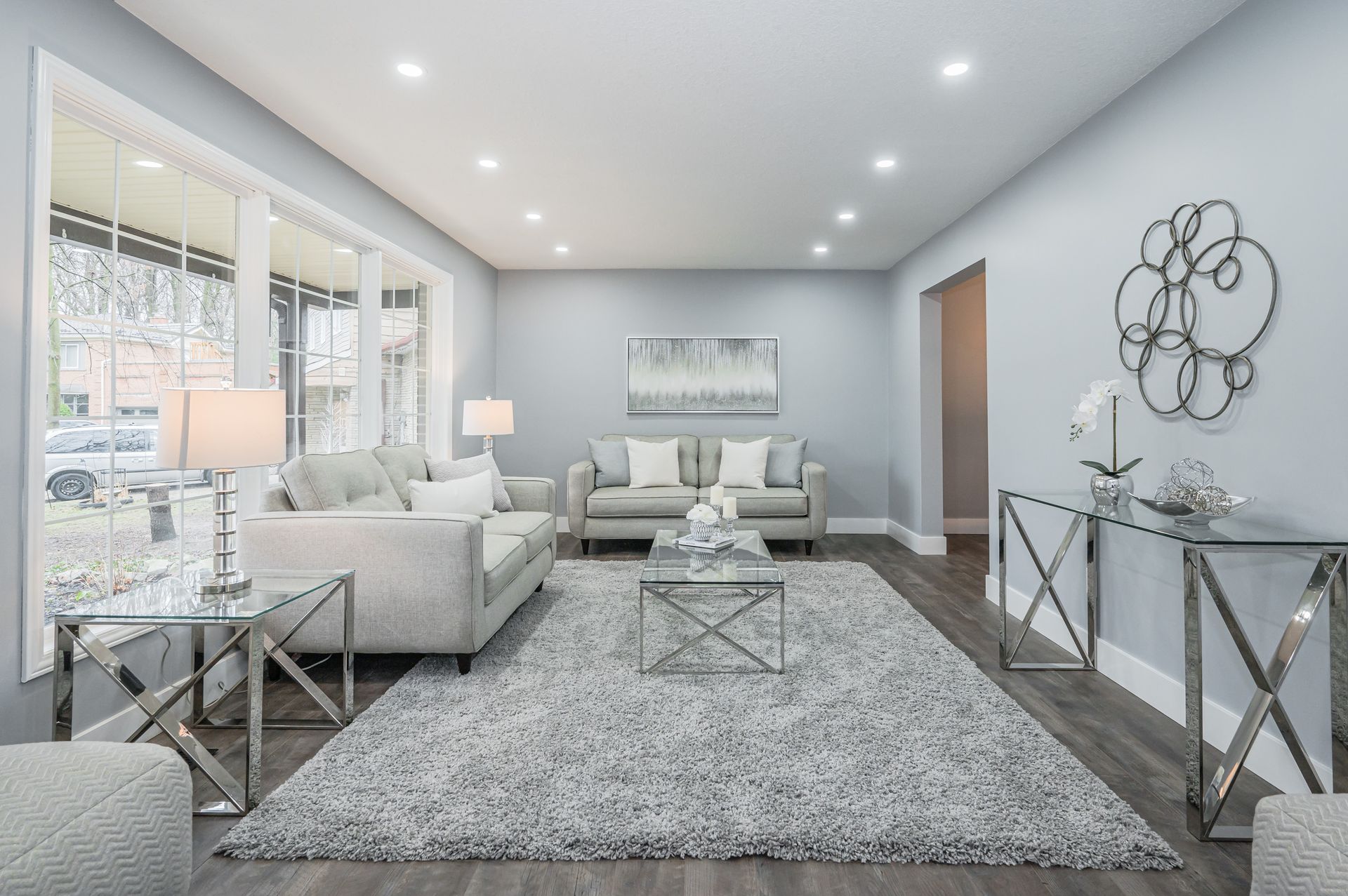 Living room with gray walls, two couches, rug, and metallic accents. Brightly lit with large windows.