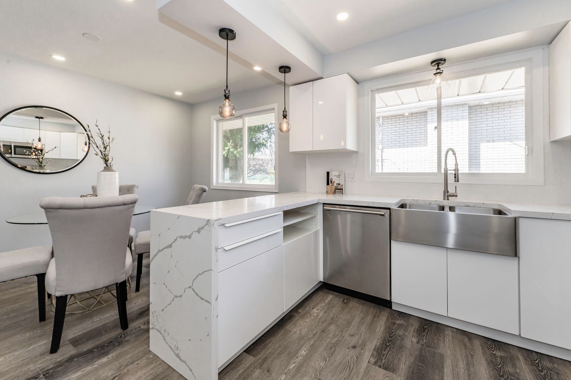 Modern white kitchen with island, stainless steel sink, and wood-look flooring.
