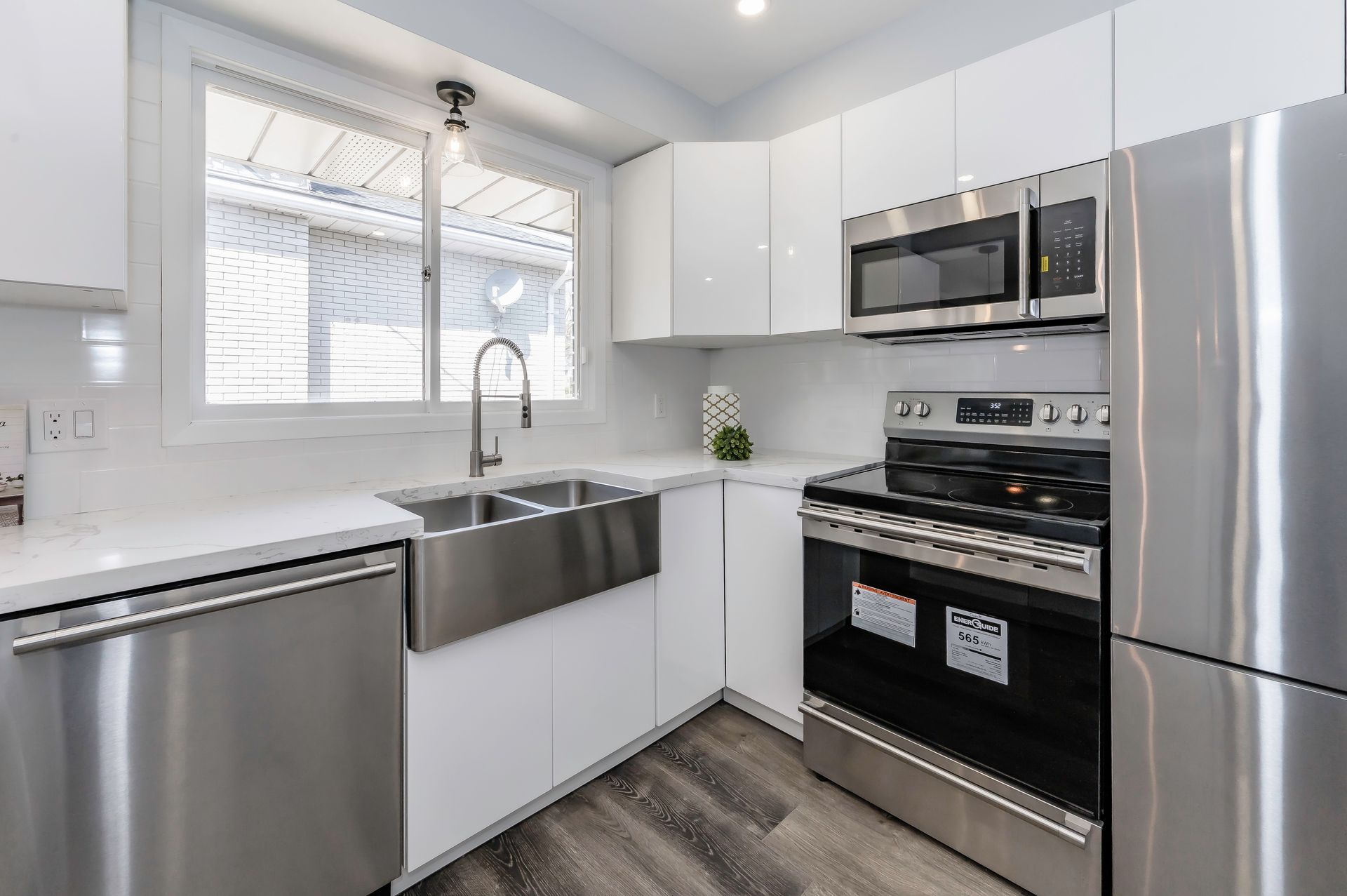 Modern white kitchen with stainless steel appliances, sink, and window.